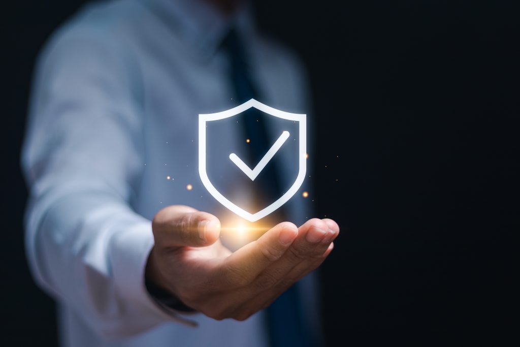 Insurance fraud prevention with a tick in a shield emblem in a man's hand.